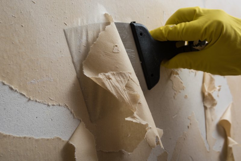 Putty knife scraping wallpaper off the wall (Photo by gogiya - stock.adobe.com)